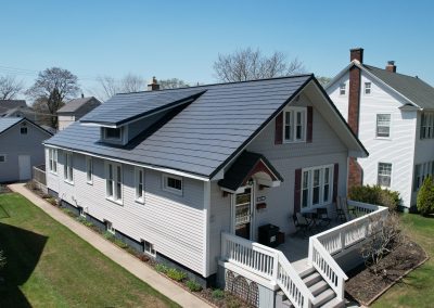 Aerial view of a historic-style home with white siding, burgundy shutters, and a charcoal gray metal roof