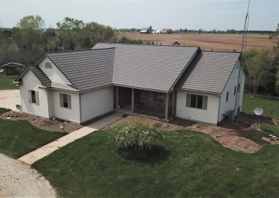Aerial view of a single-story ranch home with white vinyl siding and a charcoal gray metal roof