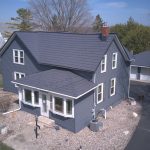 Aerial view of a two-story farmhouse with dark navy siding and a charcoal gray metal roof