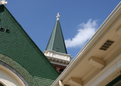 Close-up architectural view looking up at a church steeple with dark green metal shingle roofing