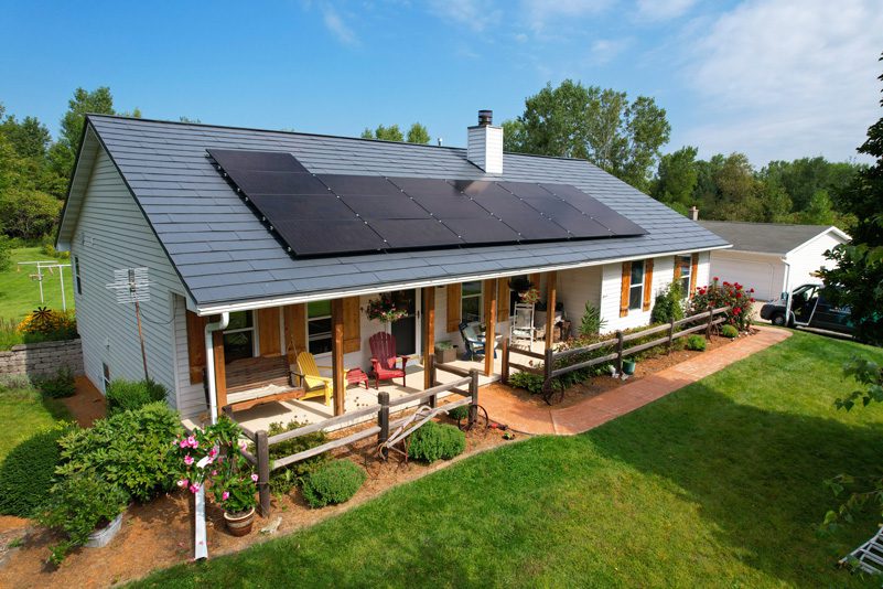 Residential solar panel installation on a ranch-style home with covered porch and lush green lawn.